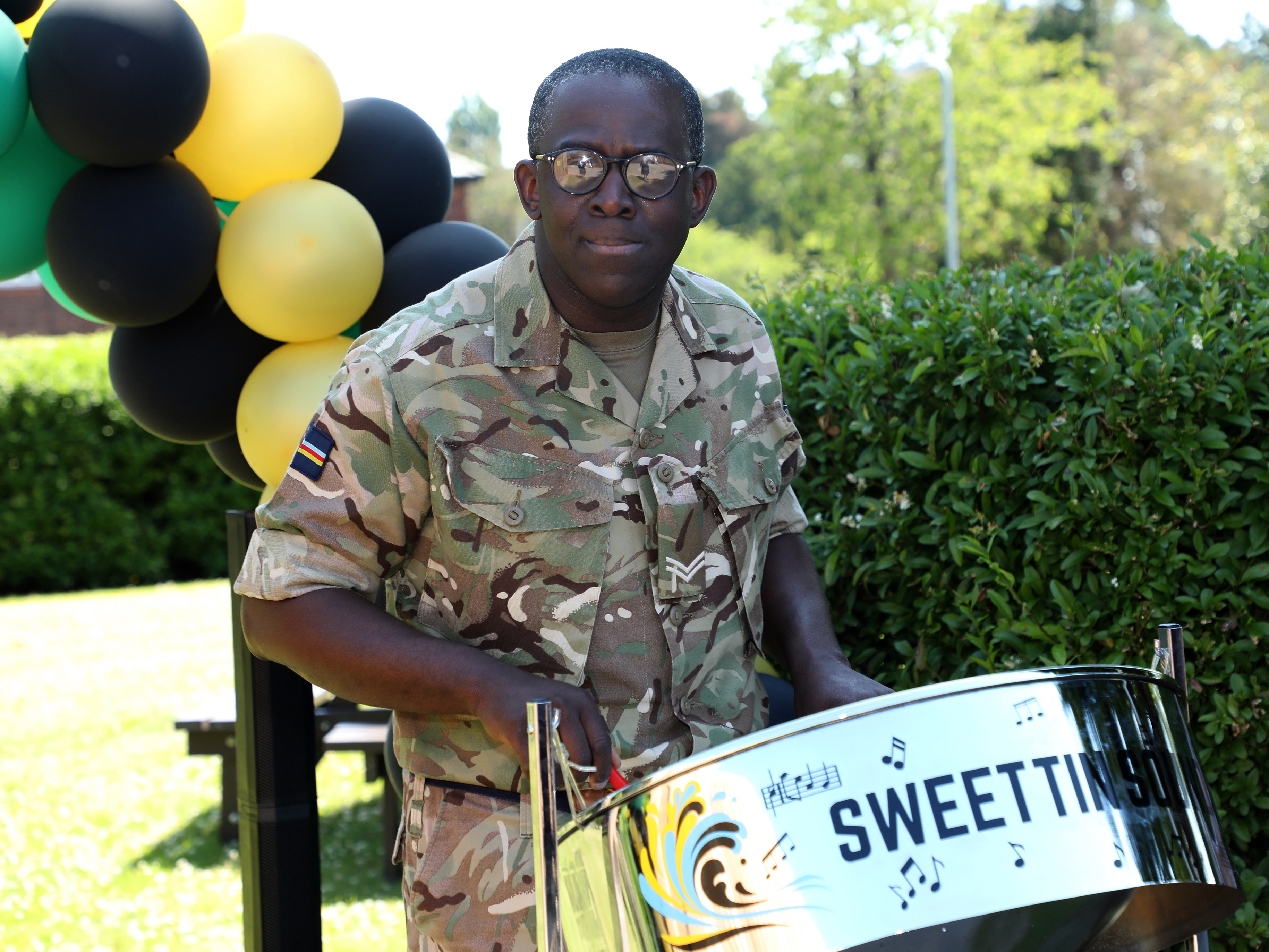 Steel drum player by arc of balloons in the colours of the Jamaican flag.